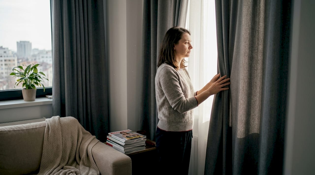 O femeie aranjează cu grijă perdelele în livingul său amenajat modern.